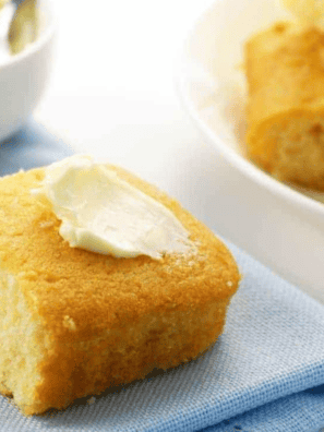 Golden slice of creamed corn cornbread baked in the air fryer, served on a plate with a pat of melting butter.