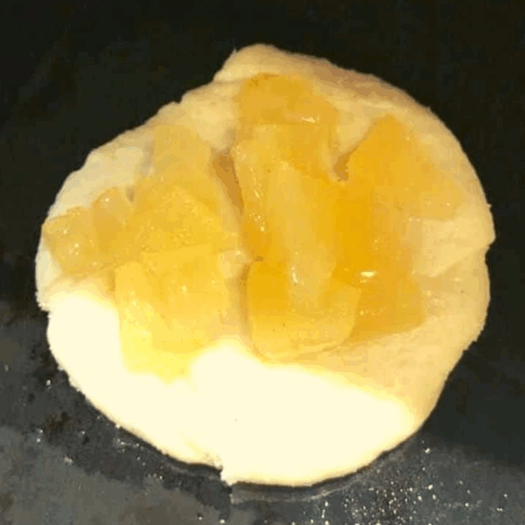 Placing dough circles onto a greased air fryer tray, adding diced apples to the center, and air frying at 330°F for 5 minutes.