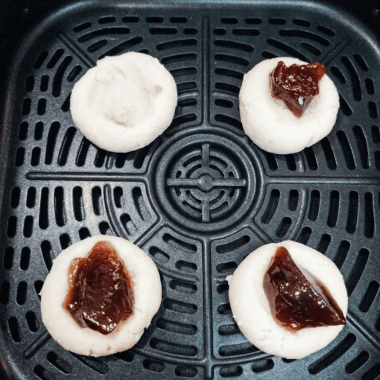 Filling each cookie well with a small spoonful of jam.