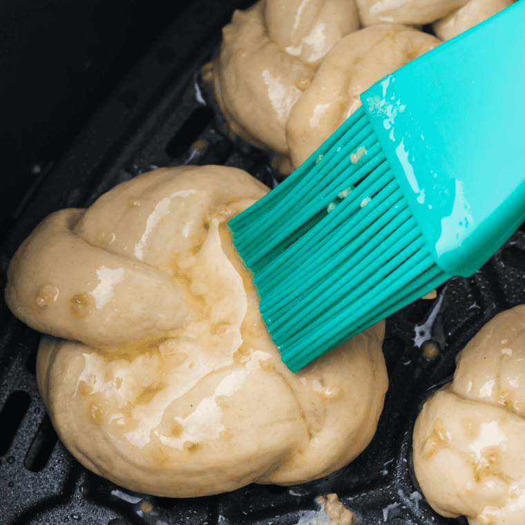 Air fryer basket filled with garlic cheddar knots in a single layer, topped with Parmesan, cheddar, and parsley.