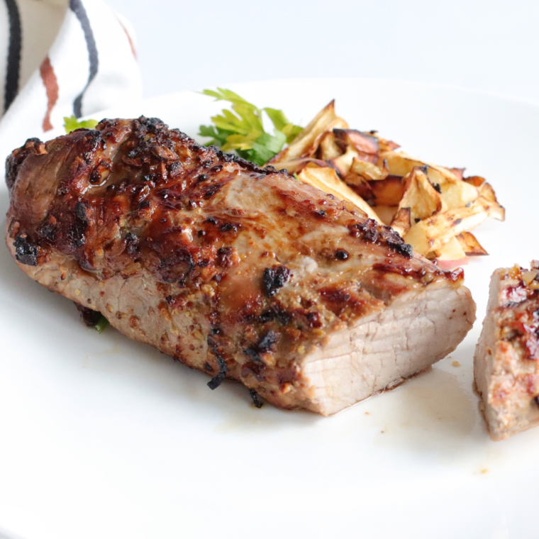 A beautifully cooked Air Fryer BBQ Pork Tenderloin glazed with barbecue sauce, sliced and served on a wooden cutting board, accompanied by fresh herbs.