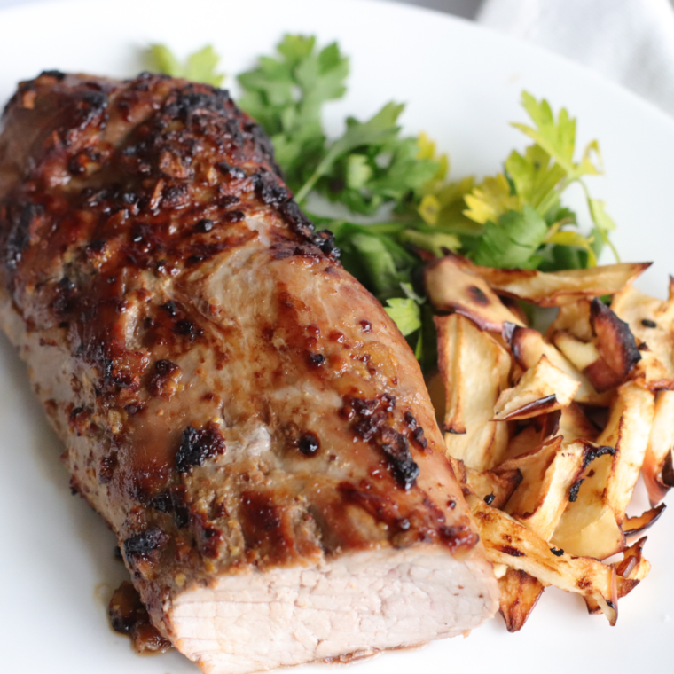 A succulent Air Fryer BBQ Pork Tenderloin glazed with barbecue sauce, sliced and served on a platter, garnished with fresh herbs.