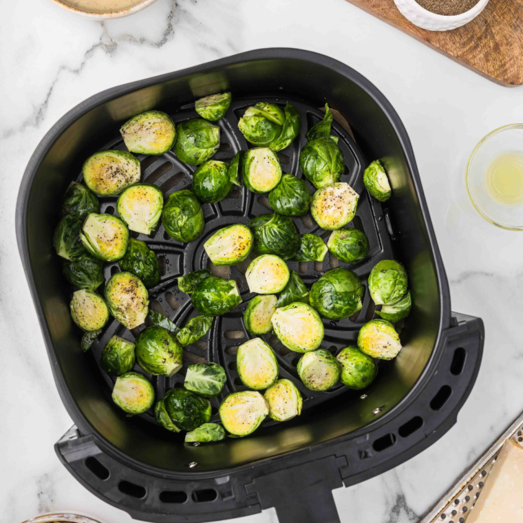 Brussels Sprouts in the air fryer basket, coated with lemon pepper seasoning.