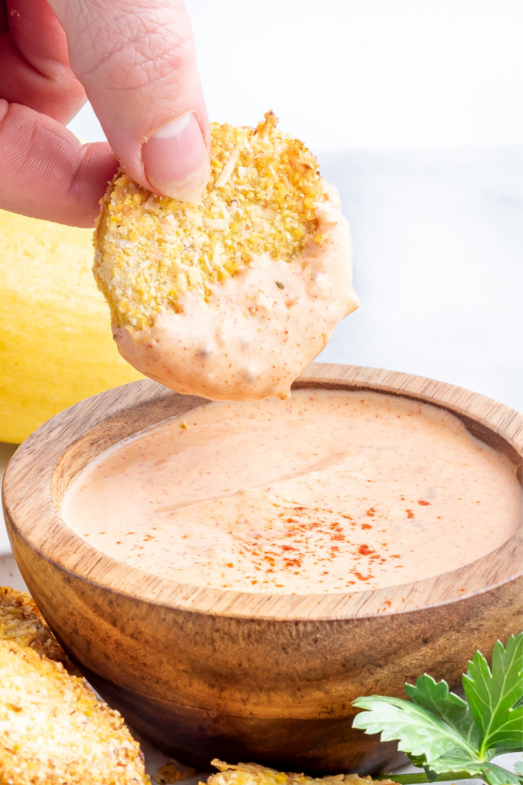 Crispy air fryer summer squash slices on a white plate with a bowl of dipping sauce