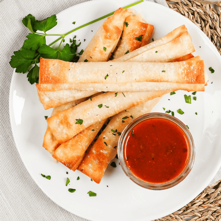 Golden brown air fryer wonton mozzarella sticks with stretchy melted cheese served beside marinara sauce.