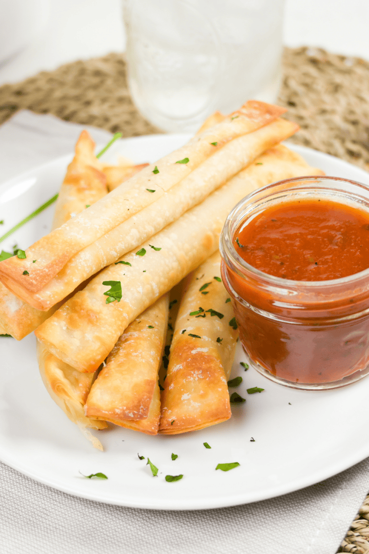 Crispy air fryer wonton mozzarella sticks stacked on a plate with melted cheese pull and marinara dipping sauce.