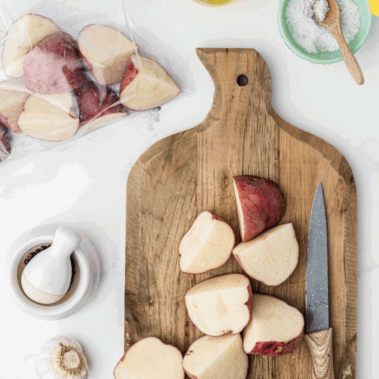 Red potatoes sliced into wedges on a cutting board beside an air fryer preheating to 375°F.