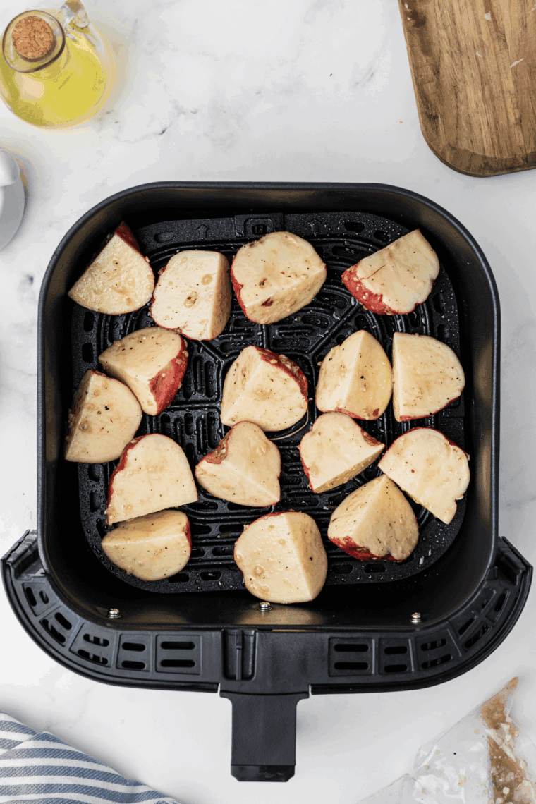 Seasoned potato wedges cooking in an air fryer basket until golden brown and crispy, ready to serve with fresh dill.