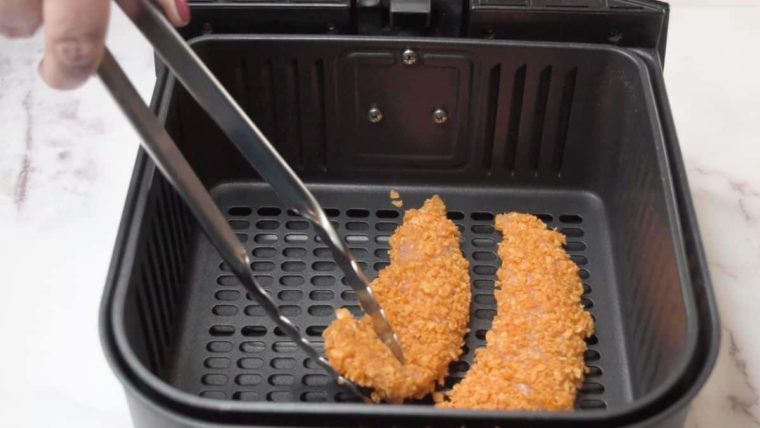 tongs adding dorito chicken strips to an air fryer basket