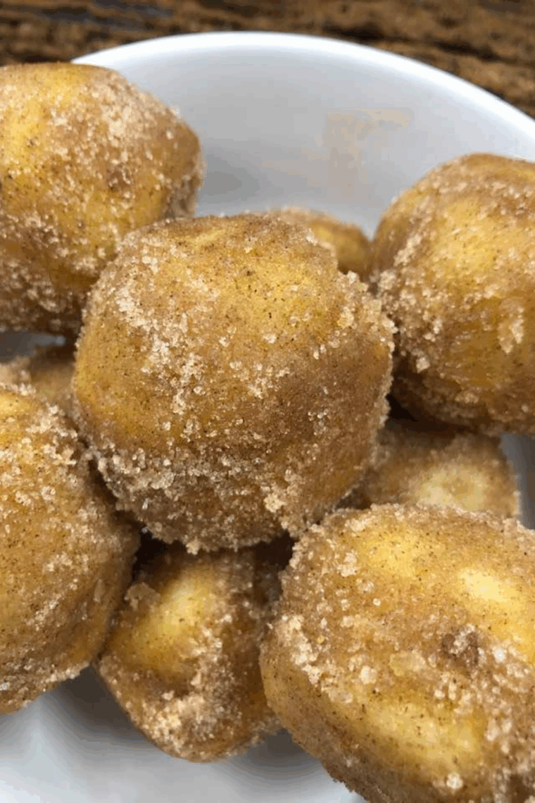 Plate of golden air fryer biscuit donut holes rolled in cinnamon sugar.