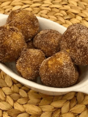 Golden air fryer biscuit donut holes coated in cinnamon sugar and served on a plate.