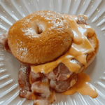 Air Fryer Cheddar Cheese Bagels stacked on a wooden board with golden melted cheddar on top and a crispy golden-brown crust.