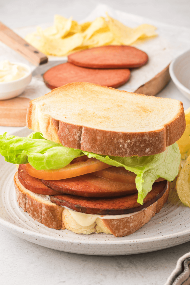 Bologna sandwich on a plate with crispy air-fried bologna, white bread, and condiments.