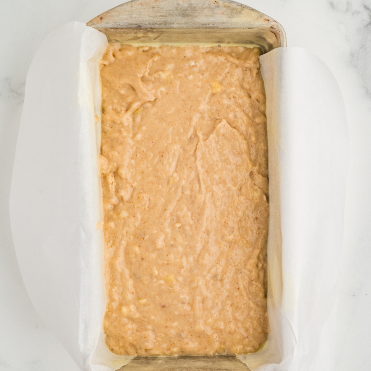 Pouring banana bread batter into a greased mini loaf pan, filling two-thirds full.