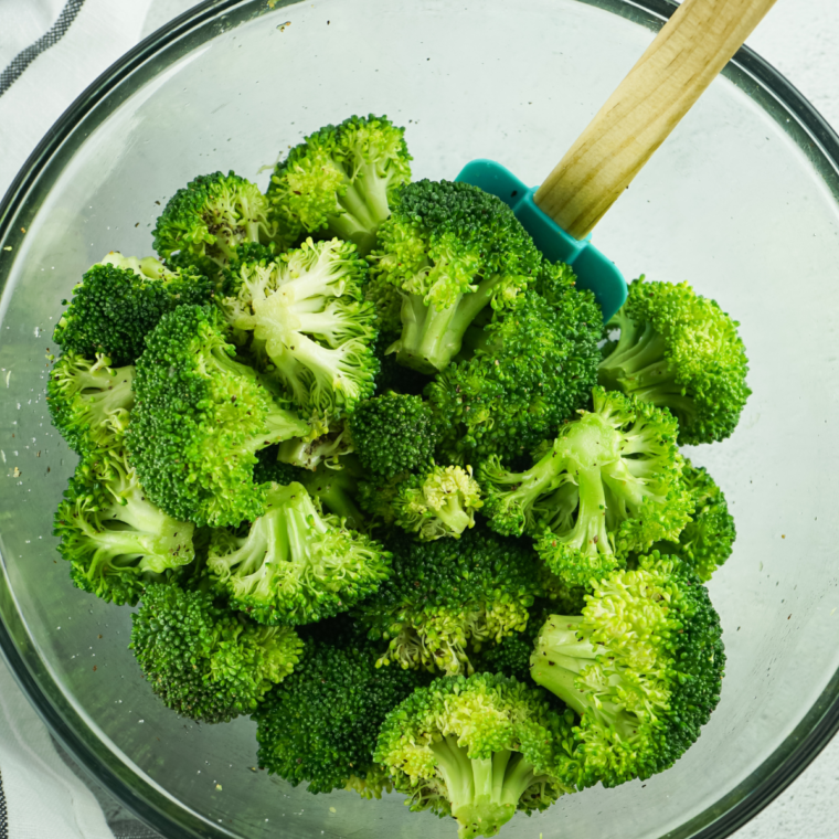 Mixing fresh broccoli florets with seasonings in a bowl, preparing for a flavorful dish.