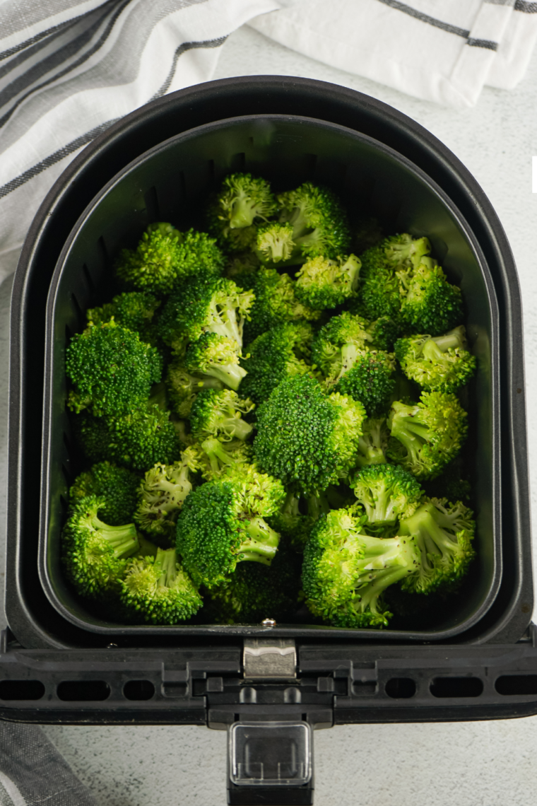 Air fryer basket filled with roasted broccoli parmesan, showcasing golden, crispy florets.