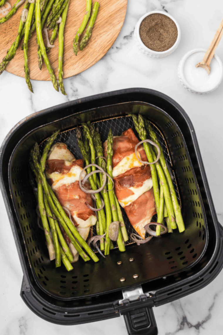Air fryer chicken saltimbocca wrapped in crispy prosciutto with sage leaves, served with asparagus and shallots on a white plate