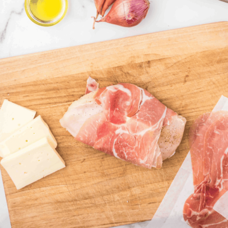 Hands wrapping prosciutto slices around chicken breast to enclose cheese and sage securely
