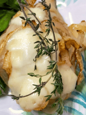 Air fryer French onion chicken breast topped with roasted onions and melted Fontina cheese on a white plate
