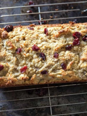 Air fryer cranberry orange nut bread loaf cooling on a wire rack, with cranberries and walnuts studding the golden top