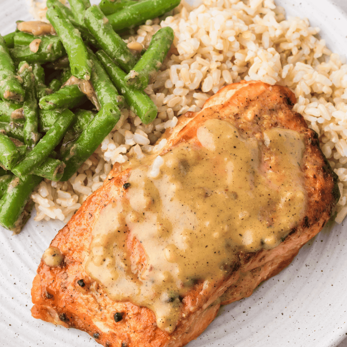 Golden-brown air fryer frozen salmon fillets served on a plate with rice and green beans.