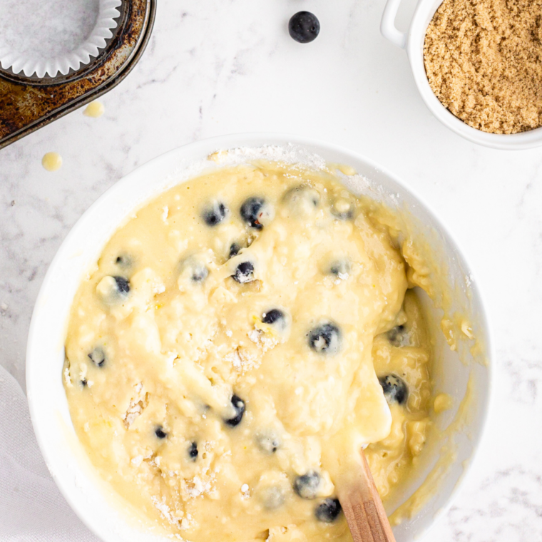 Floured blueberries being added to pound cake batter in a mixing bowl