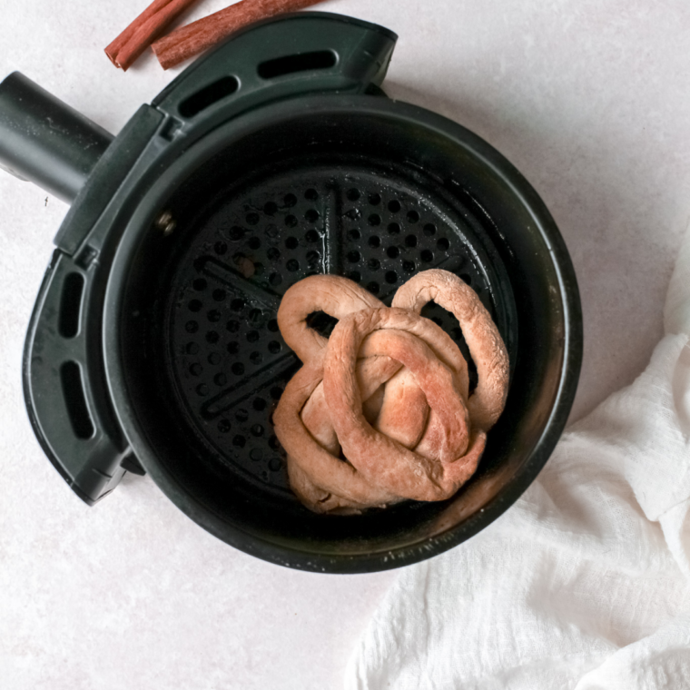 Golden brown funnel cake cooking in an air fryer basket after being flipped halfway through