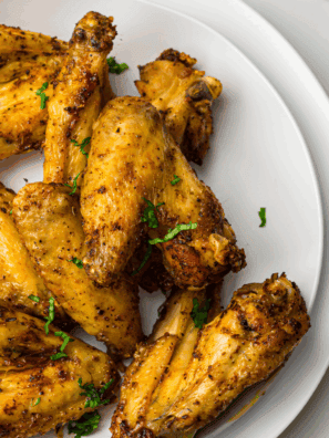 Golden-brown air fryer chicken wings coated in a glossy honey mustard sauce, served on a white plate with a side of dipping sauce.