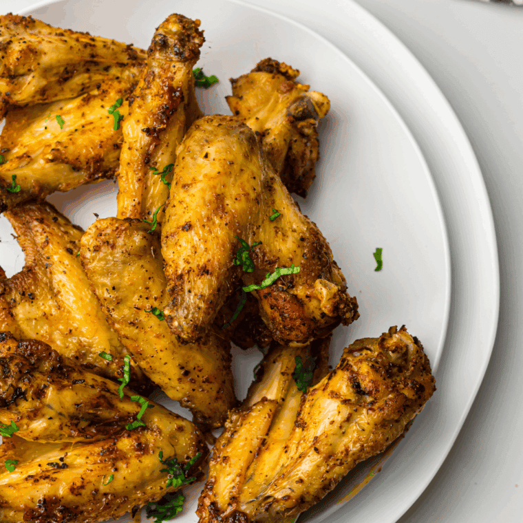 Golden-brown air fryer chicken wings coated in a glossy honey mustard sauce, served on a white plate with a side of dipping sauce.
