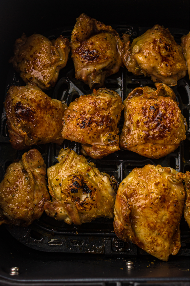Cooked pesto chicken thighs in an air fryer basket with browned, crisp edges