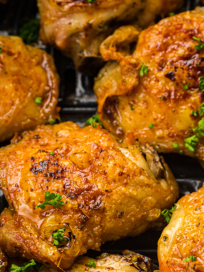Air fryer pesto chicken thighs in a black air fryer basket, coated in green basil pesto with browned crisp edges