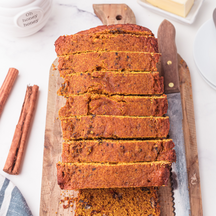 A thick slice of pumpkin nut bread with salted butter beside a cup of black coffee