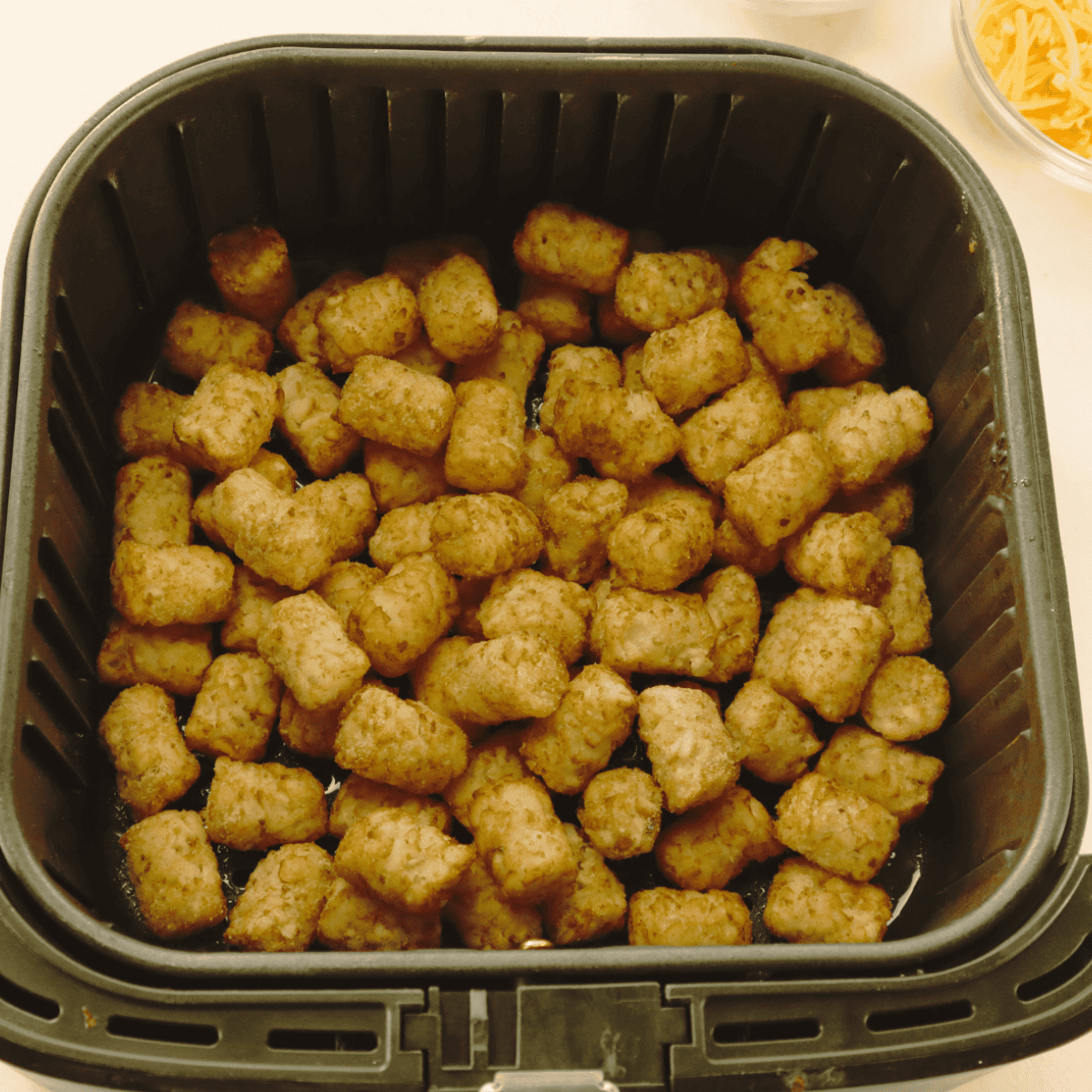 Cooking Copycat Domino’s Cheddar Bacon Loaded Tots in the air fryer basket.