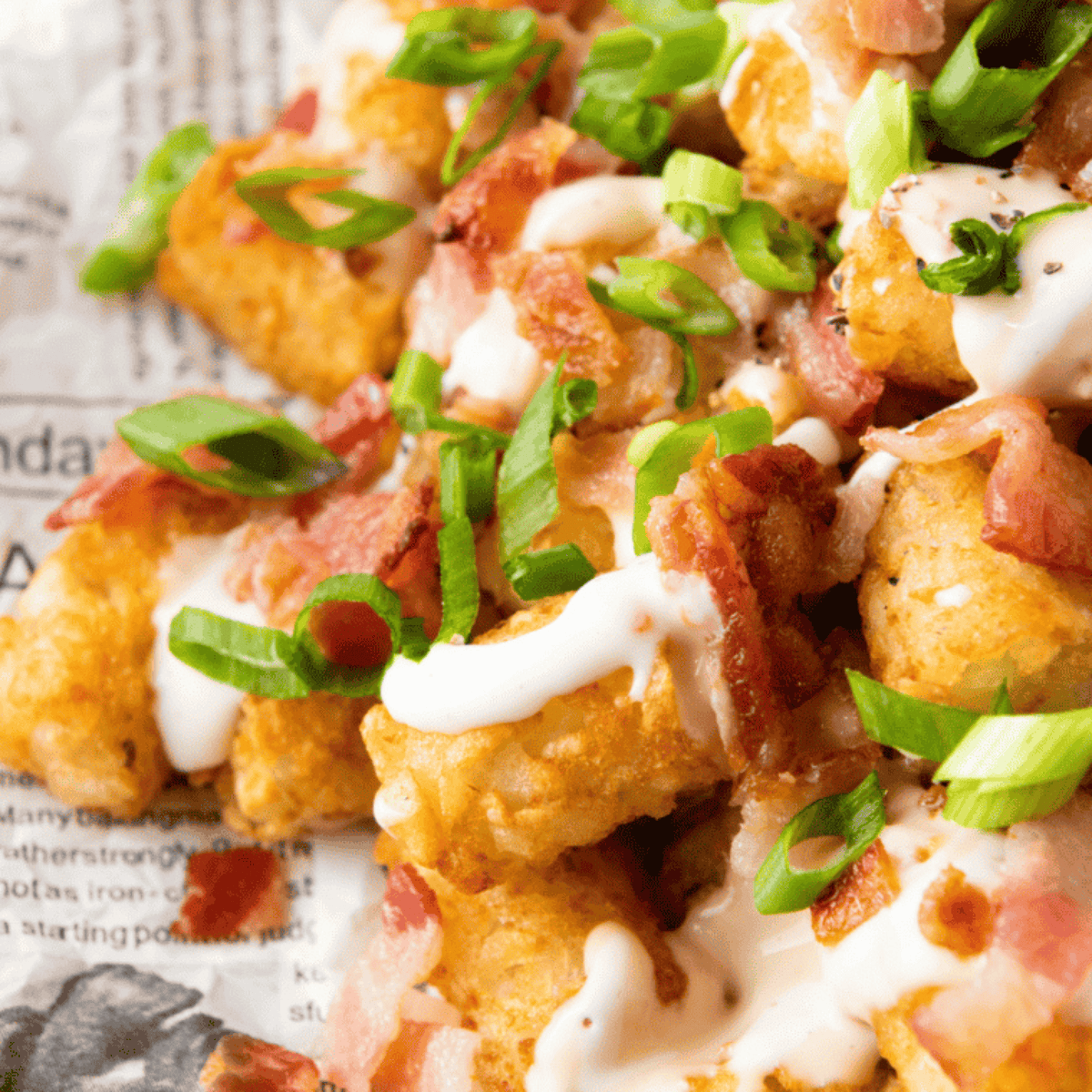 Air fryer cheddar bacon loaded tater tots topped with melted cheese and crispy bacon, surrounded by small bowls of toppings.