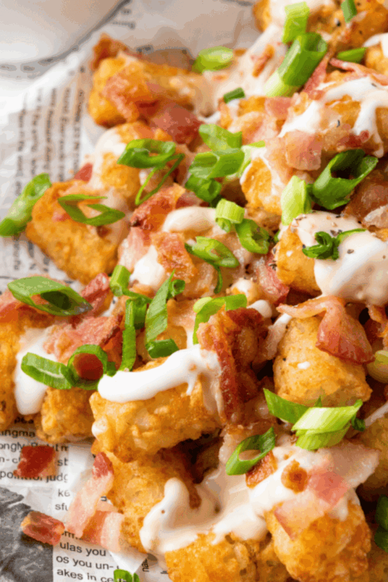 Close-up of crispy cheddar bacon loaded tater tots topped with melted cheese and bacon bits on a serving plate.