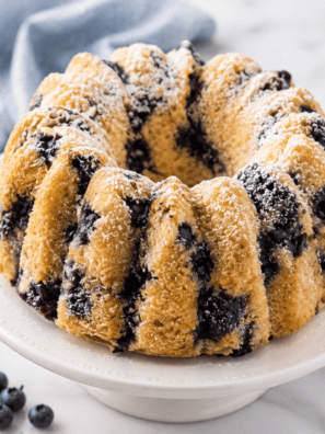 Copycat Nothing Bundt Cakes lemon blueberry bundt cake with piped cream cheese frosting ribbons, one slice cut to show blueberries in the crumb