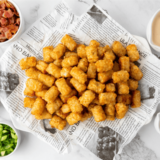 Homemade copycat Taco John's Potato Olé seasoning in a glass jar beside a bowl of crispy seasoned tater tots