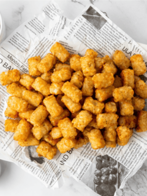 Homemade copycat Taco John's Potato Olé seasoning in a glass jar beside a bowl of crispy seasoned tater tots