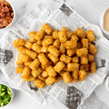 Homemade copycat Taco John's Potato Olé seasoning in a glass jar beside a bowl of crispy seasoned tater tots