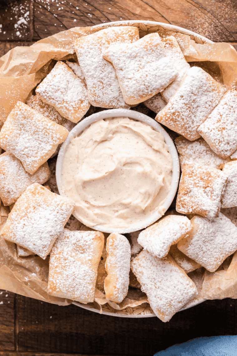 A serving plate piled high with golden, puffy Air Fryer Puff Pastry Beignets dusted heavily with white powdered sugar.