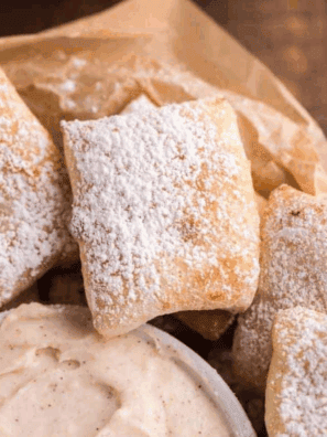 A serving plate piled high with golden, puffy Air Fryer Puff Pastry Beignets dusted heavily with white powdered sugar.