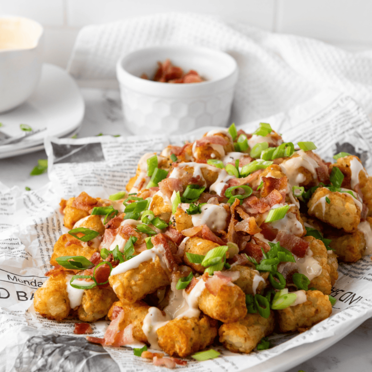 loaded tater tots from air fryer with sour cream, cheese, bacon, and green onion on top