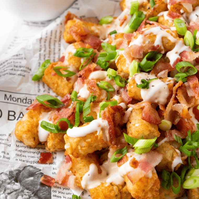 closeup: loaded tator tots in air fryer with bacon, sour cream, and green onion on top