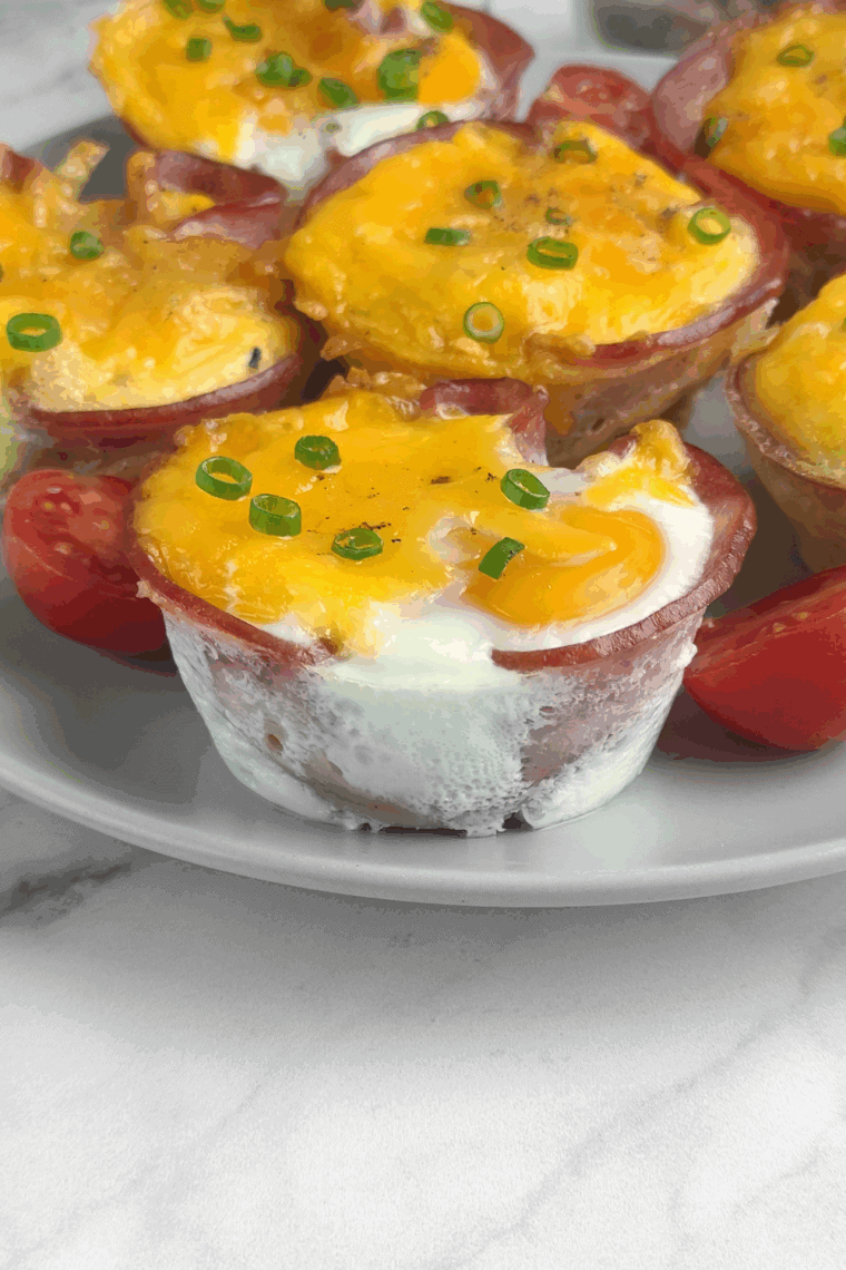 Air fryer ham and egg cups made with ham slices, eggs, melted cheese, and green onions in a muffin pan