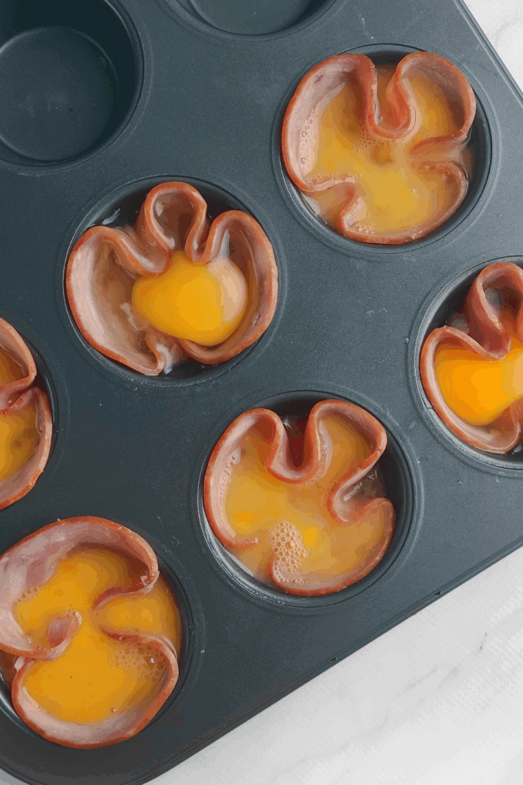 Golden-brown air fryer ham and egg cups garnished with fresh chives on a white plate.