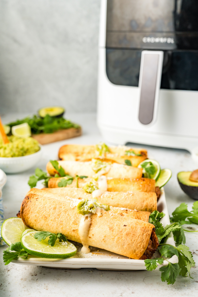 Crispy air fryer beef and bean taquitos filled with seasoned beef, refried beans, and melted cheese served with dipping sauce and toppings