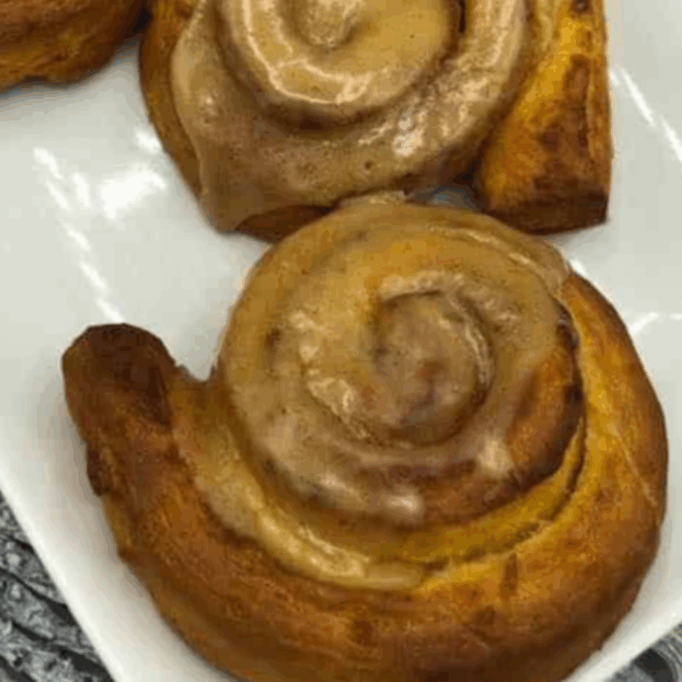 Freshly air-fried pumpkin cinnamon rolls topped with icing on a plate.