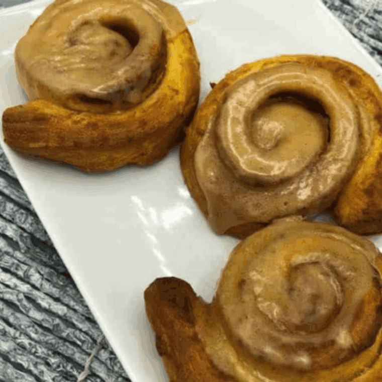 Pumpkin cinnamon rolls made in the air fryer with creamy glaze.