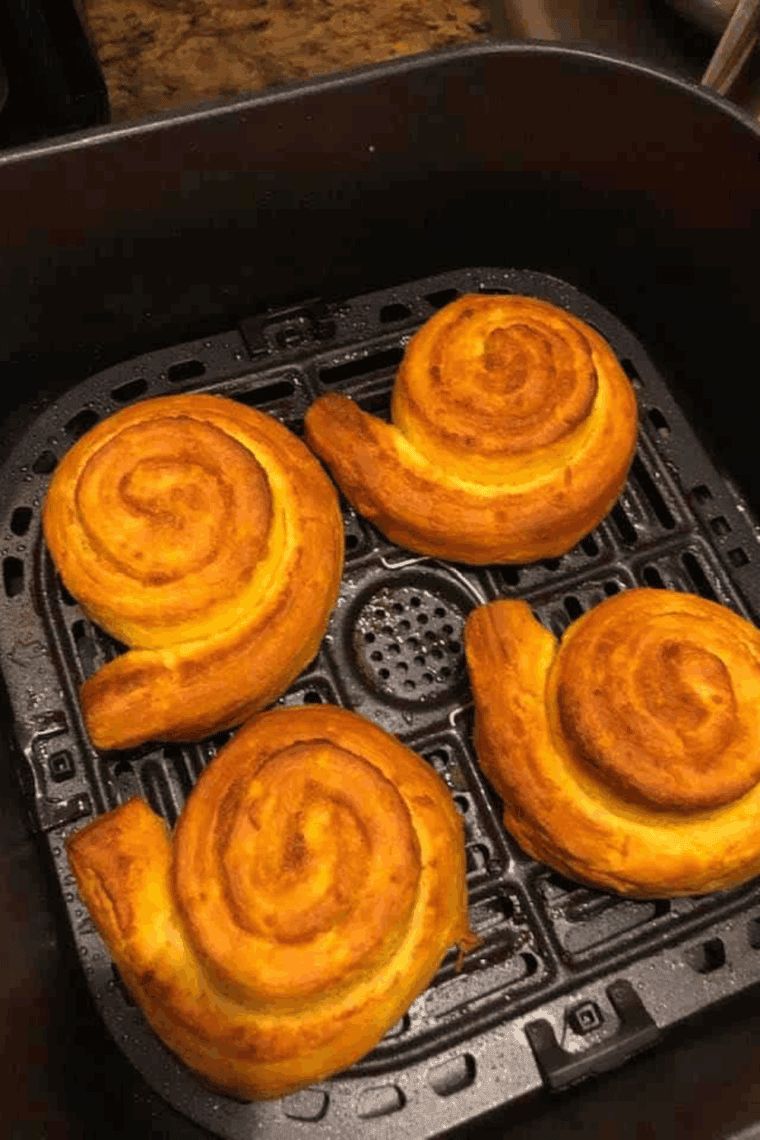 Cooked cinnamon rolls in the air fryer basket.