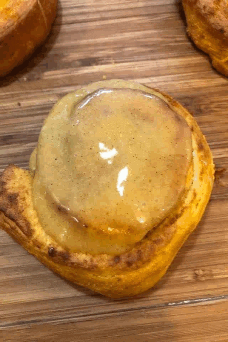 Air Fryer canned pumpkin cinnamon rolls topped with sweet glaze on a white plate.